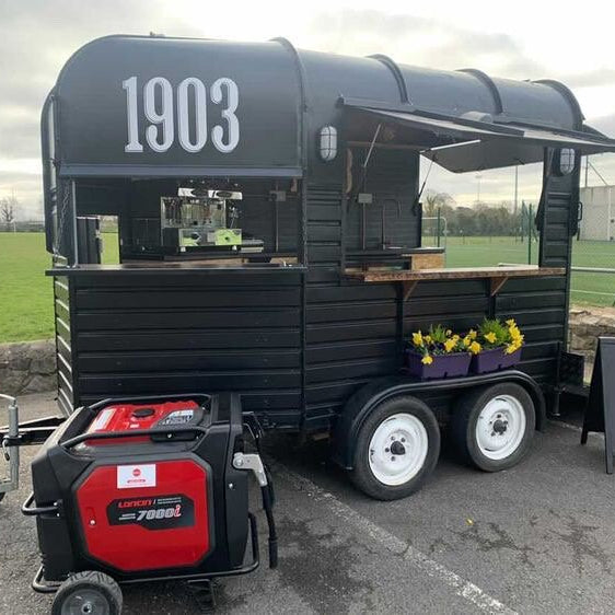 Black food truck with '1903' branding on a paved area with a field in the background. Running on Power from a Loncin Generator Hired from Dalys Tool Hire